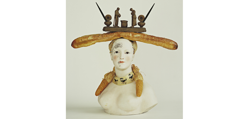 porcelain bust of a woman, with a large baguette and bronze statue precariously set on her head